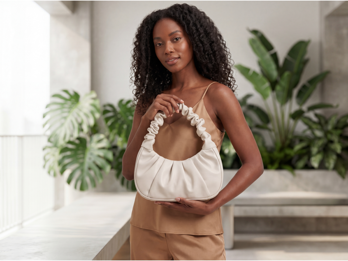 Mulher com cabelos cacheados segurando bolsa hobo  franzida off-white Lundiar em varanda com plantas  tropicais &mdash; look casual sofisticado bege e caramelo